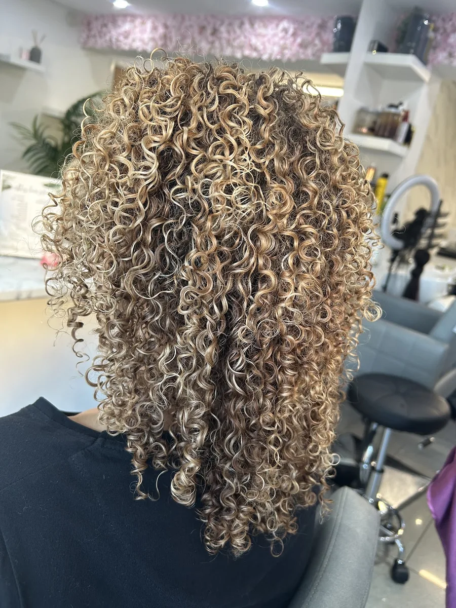 Tight blonde highlighted curls with a deliberate dark root